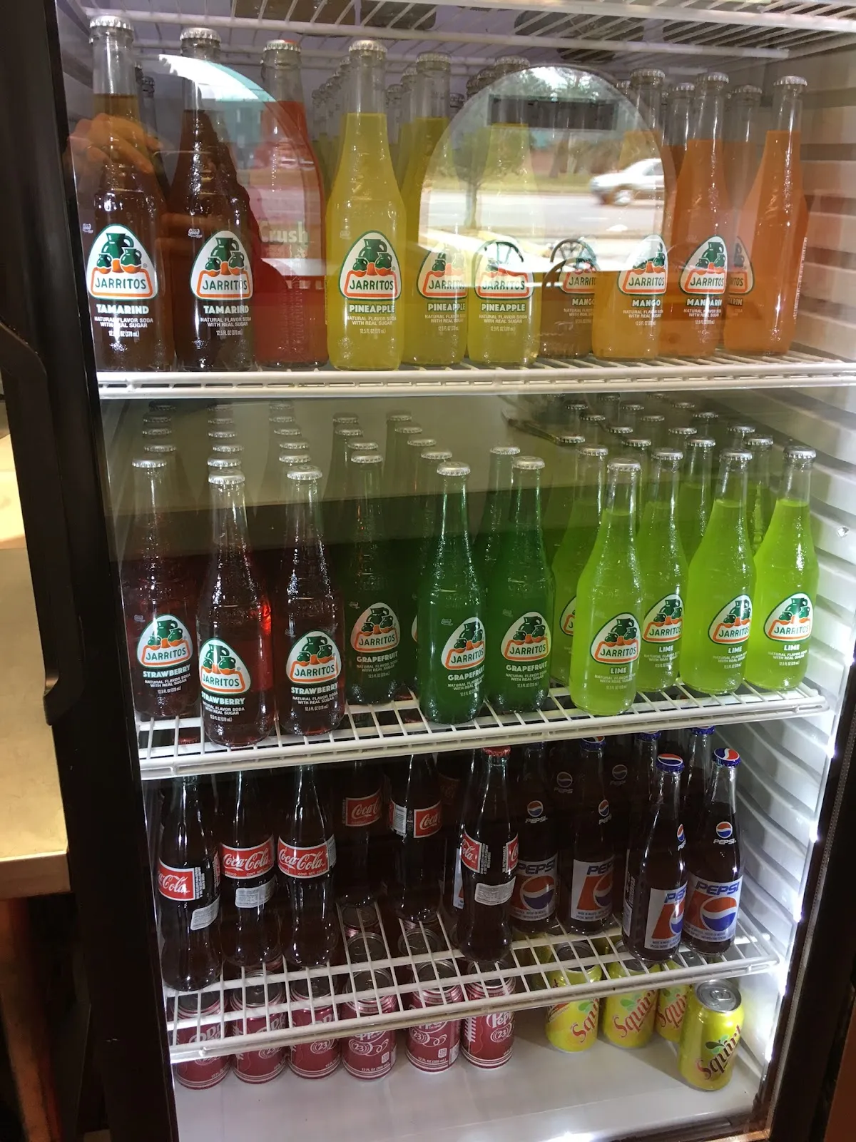 Cooler stocked with Jarritos Mexican fruit sodas, Coca-Cola, Pepsi, and Squirt