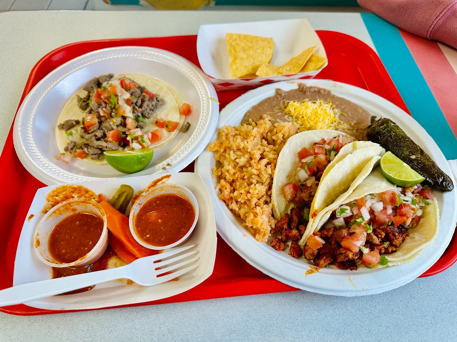 Carne asada tacos with Spanish rice, refried beans, chips, salsa, and a roasted jalapeno on a red tray